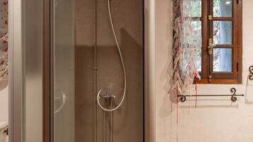 Une salle de bain avec une douche à parois de verre, une porte en bois et une fenêtre ornée de rideaux à motifs floraux.