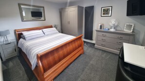 A bedroom with a wooden bed, a dresser, a mirror, a radiator, and a TV on the wall. - The Nook is a cosy holiday let in Rostrevor at the foot of the Mourne mountains. (Rostrevor)