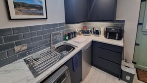 A compact kitchen with dark blue cabinets, a marble countertop, a dishwasher, a coffee maker, and a toaster. - The Nook is a cosy holiday let in Rostrevor at the foot of the Mourne mountains. (Rostrevor)