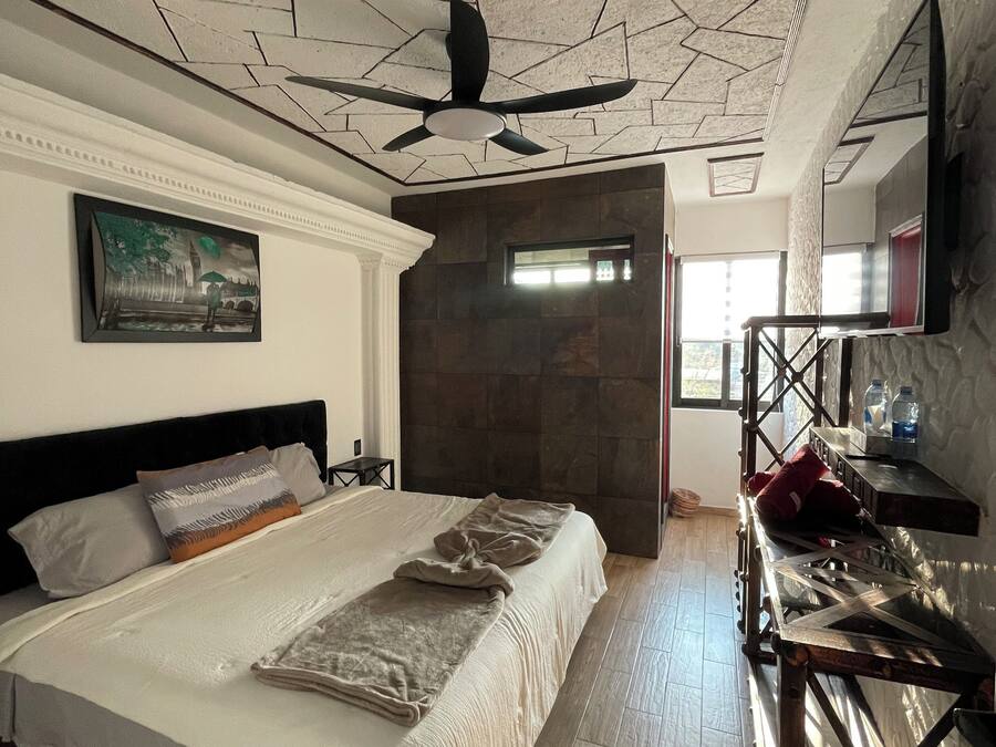 A bedroom with a bed, a ceiling fan, a painting, and a wooden floor.