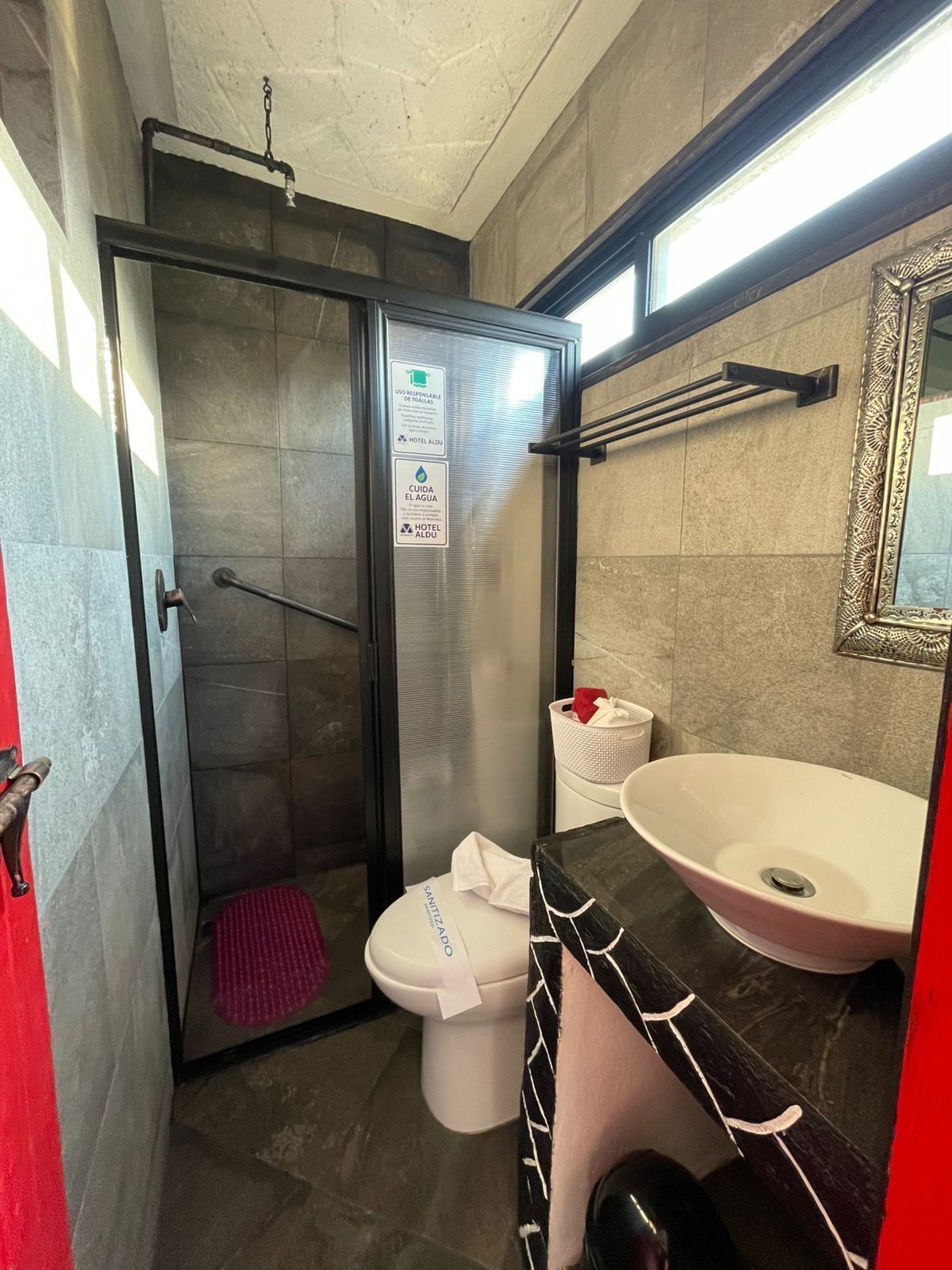 Ein Badezimmer mit Dusche, Toilette und Waschbecken. An den Wänden befinden sich Schilder und über dem Waschbecken ein Spiegel.