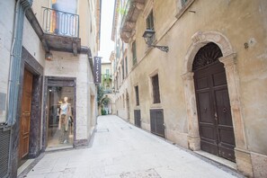A narrow street with buildings on either side, featuring a shop with a mannequin display and a large, ornate door. - Italianflat - Via Mazzini (Verona)