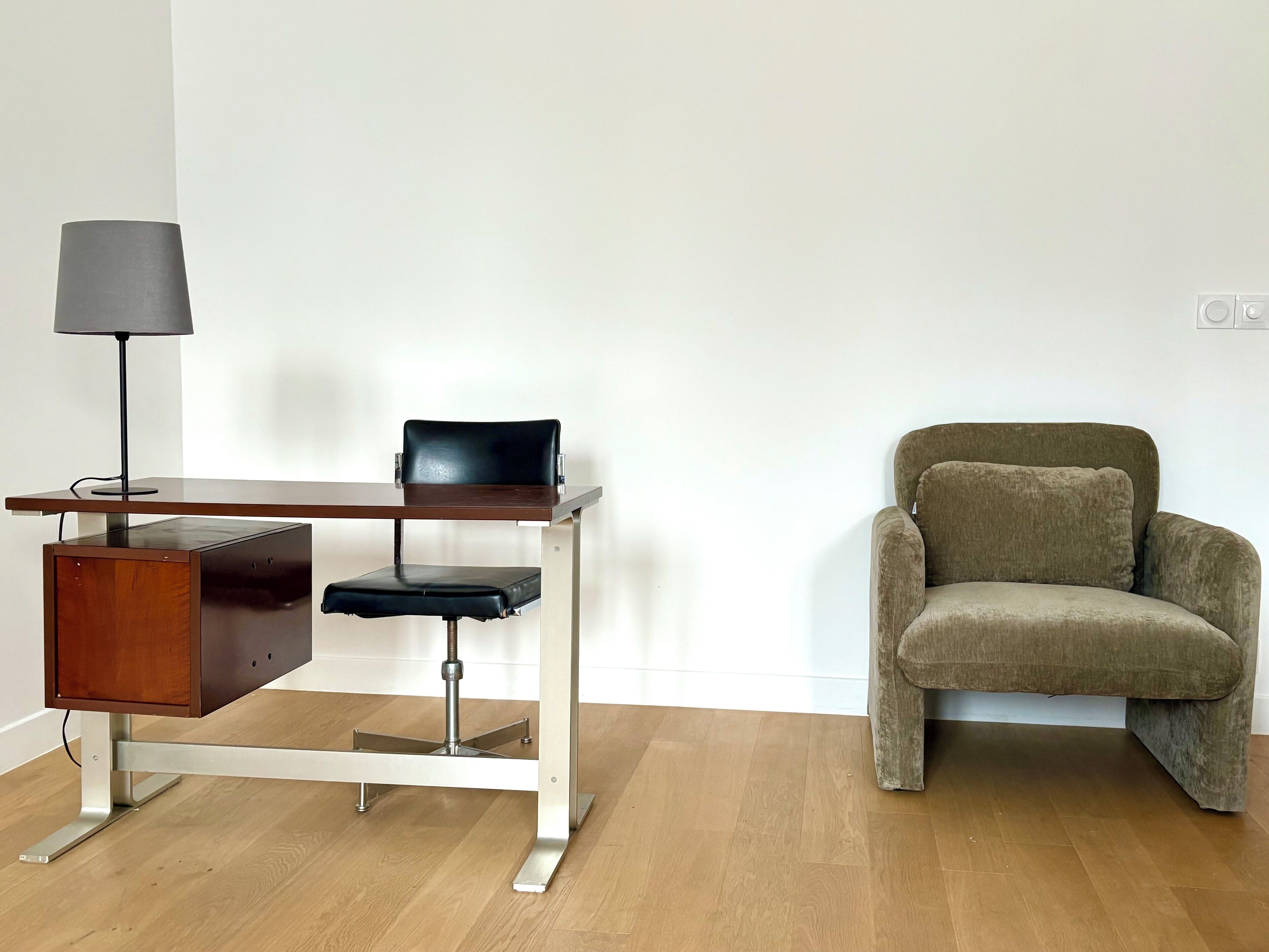 Un escritorio moderno con una silla, una lámpara y un sillón tapizado en una habitación de estilo minimalista.