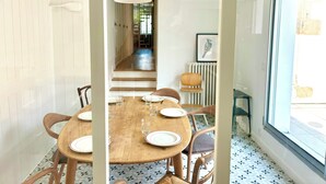 A dining area with a wooden table set for six, surrounded by chairs. A large window provides natural light, and a staircase leads to an upper level. - Large duplex with garden in Auray town center (Auray)