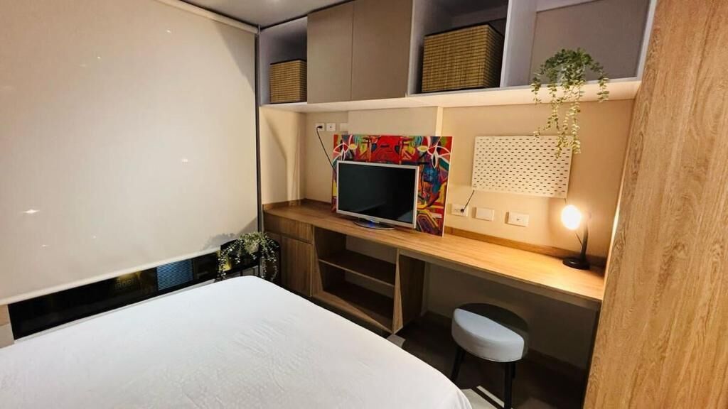 Un dormitorio moderno con una cama grande, un escritorio con una computadora y un televisor.