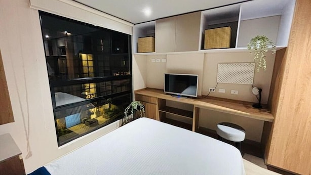 Een moderne slaapkamer met een groot bed, een bureau met een computer en een raam met uitzicht op een stadsgezicht.
