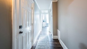 A hallway with white doors, a patterned rug, and a view into a room with a window. - Stately State Street Abode 2 (Bowling Green)