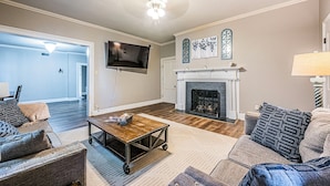 A living room with a fireplace, a television mounted on the wall, and a ceiling fan. - Stately State Street Abode 2 (Bowling Green)