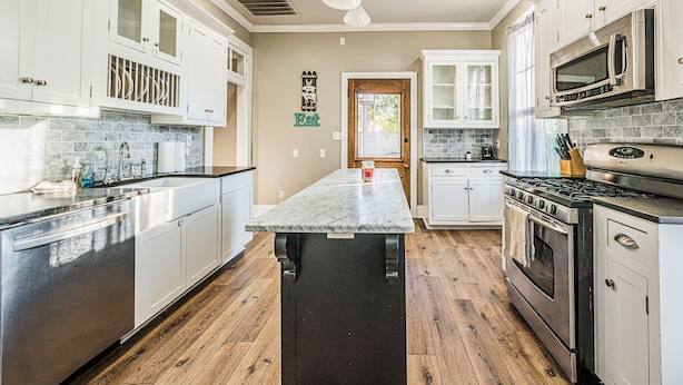 A modern kitchen with white cabinets, a central island, stainless steel appliances, and a wooden floor. - Stately State Street Abode 2 (Bowling Green)