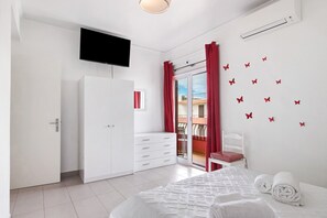 A bedroom with a bed, a wardrobe, a television, a sliding glass door to a balcony, and butterfly decals on the wall.