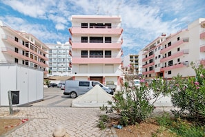 A multi-story residential building with balconies, a paved courtyard, and parked cars.