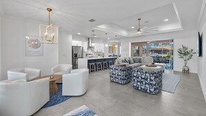 Un salon moderne avec des meubles blancs, une cuisine à l’arrière-plan et une vue sur l’extérieur.