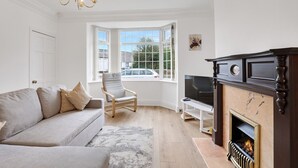 En stue med sofa, lænestol, pejs, fjernsyn og store vinduer.
