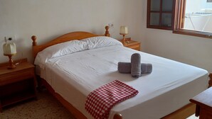 A neatly made bed with a checkered blanket, a bedside lamp, and a window with a view of the outside.