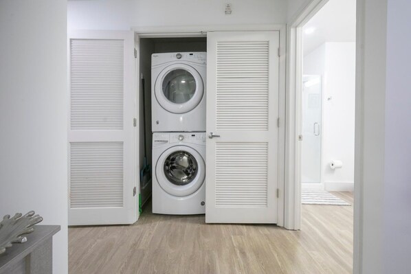A laundry room with a front-loading washer and dryer, a door with a handle, and a wooden floor. - The Rebel Ridge, 1 blk off Sq, Velvet Ditch Villas (Oxford)