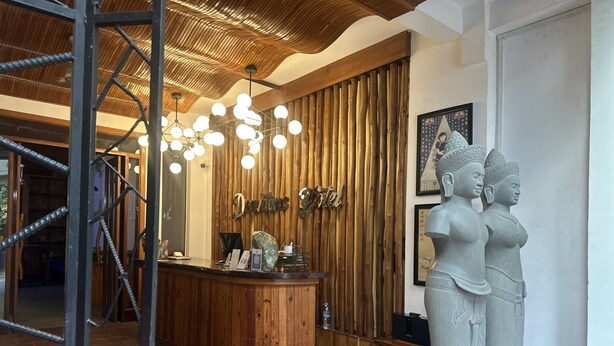 Uma área de recepção com um balcão de madeira, um lustre moderno e uma estátua de duas figuras.