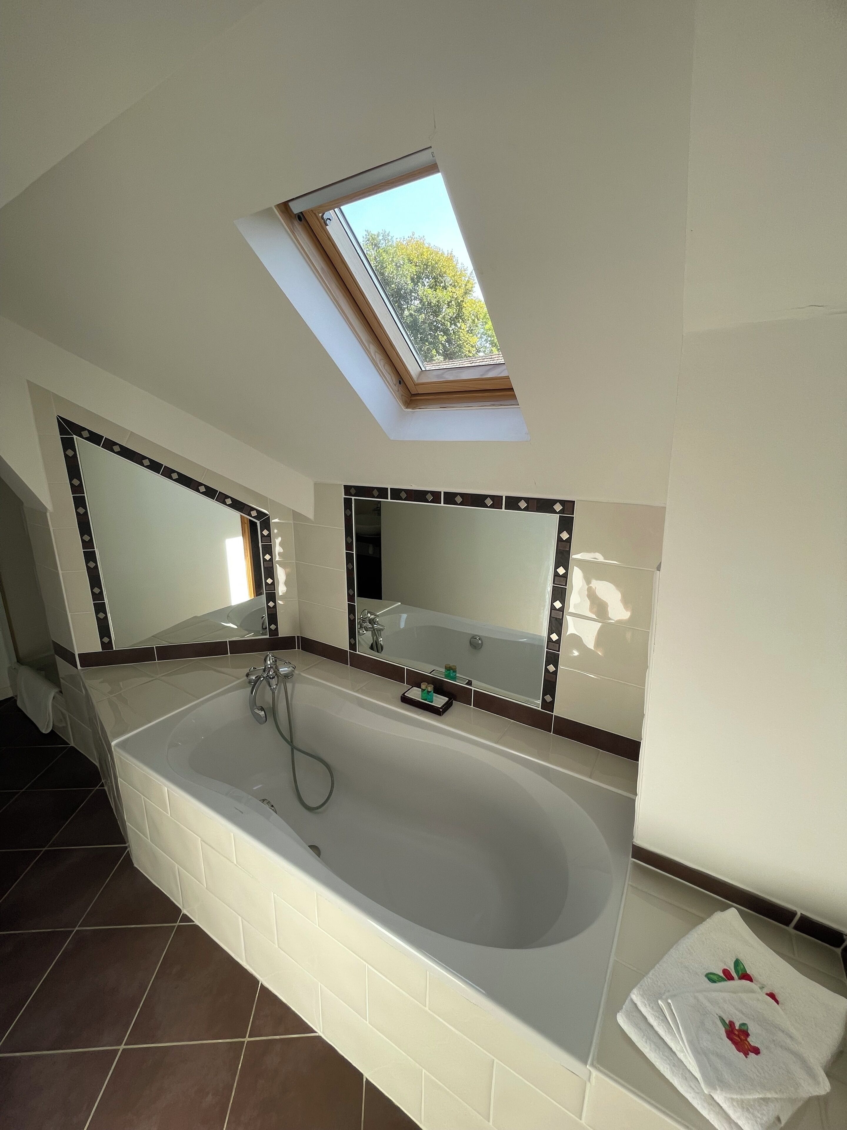 Een badkamer met dakraam, een groot bad en een spiegel boven het bad.