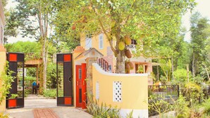 A gated entrance with a yellow wall, a red door, and a tree with fruit. - Spacious View House 2BR (Hue)