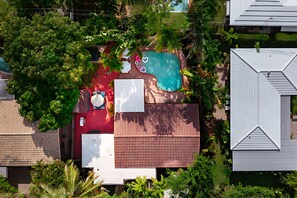 Vista aérea de una propiedad residencial con piscina, un deck rojo y un área cercada.