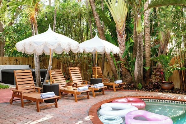 Un área junto a la piscina con sillones de madera, toldos blancos y flotadores hinchables.