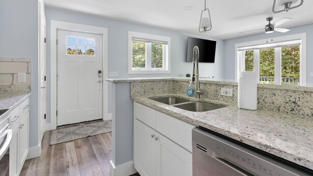 A modern kitchen with granite countertops, a double sink, and a dishwasher. There are two windows providing natural light and a door leading to another room. - Private & Quiet Retreat Near Folly Beach (Charleston)