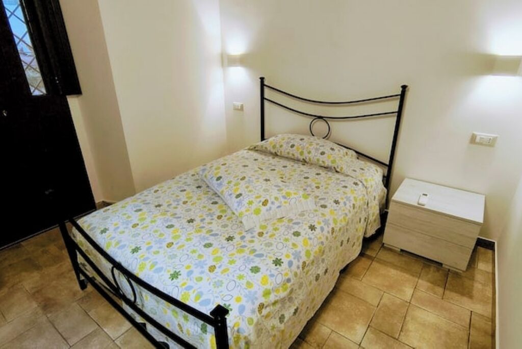 A single bed with a metal frame, a bedside table with a drawer, and a wall-mounted light fixture.