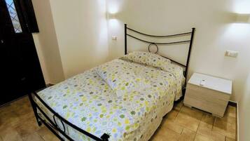 A single bed with a metal frame, a bedside table with a drawer, and a wall-mounted light fixture.