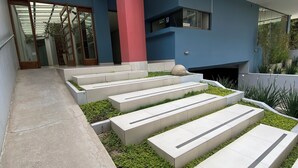 A modern building with a glass entrance, a red pillar, and a series of steps leading to a garden area. - Beautiful apartment with incredible view. Super spacious, comfortable and full of light (Cochabamba)