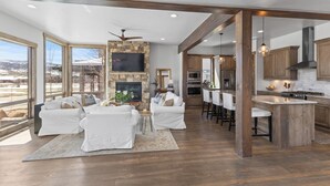 A spacious living area with a fireplace, white sofas, and a large window overlooking a snowy landscape.