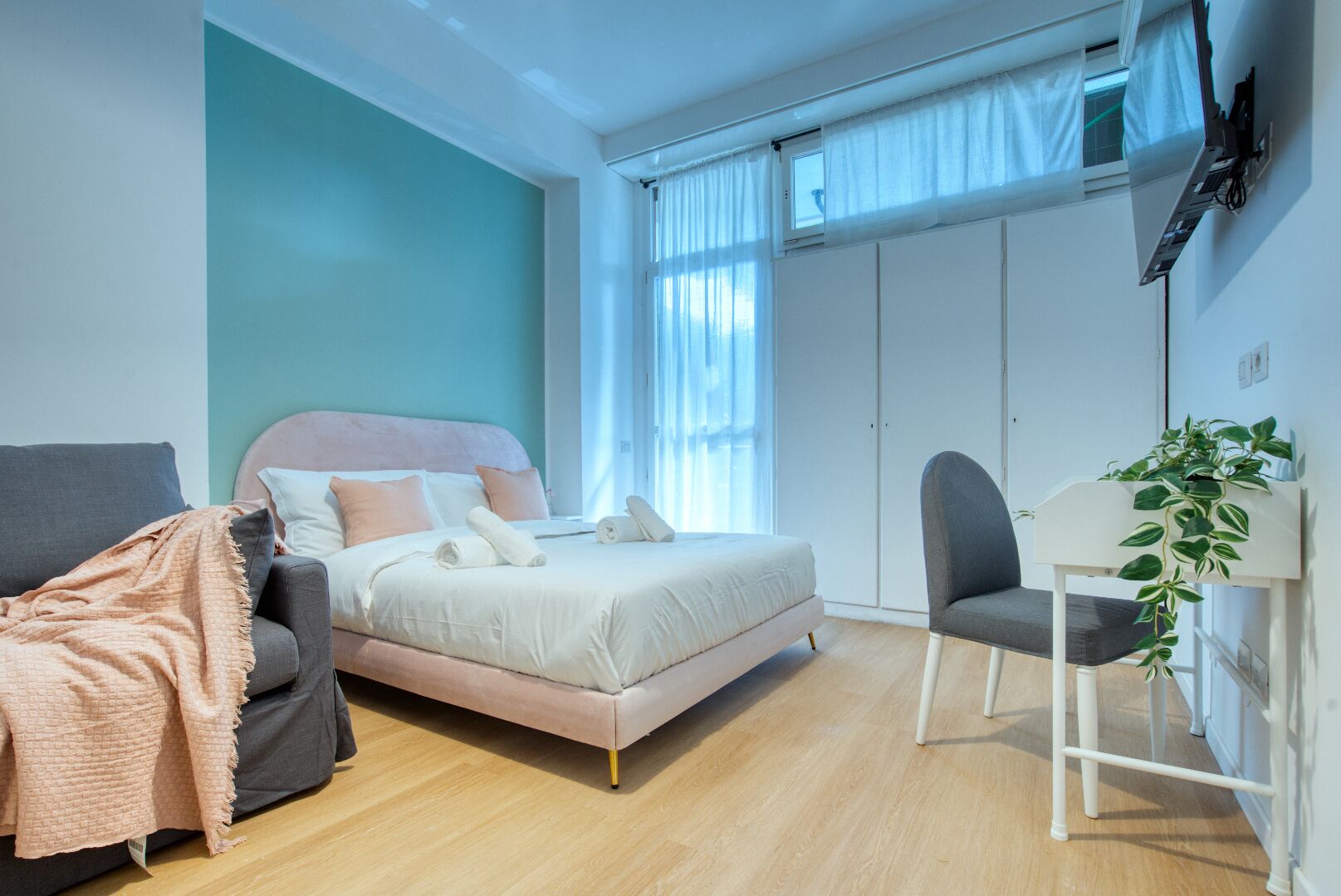 A bedroom with a bed, a chair, a desk, and a plant.
