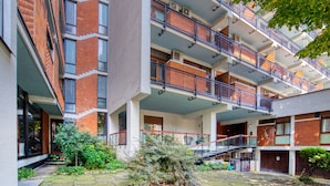 A multi-story residential building with balconies, a central courtyard with stone paving, and surrounding greenery. - Italianflat - Elegant Suites (Milan)