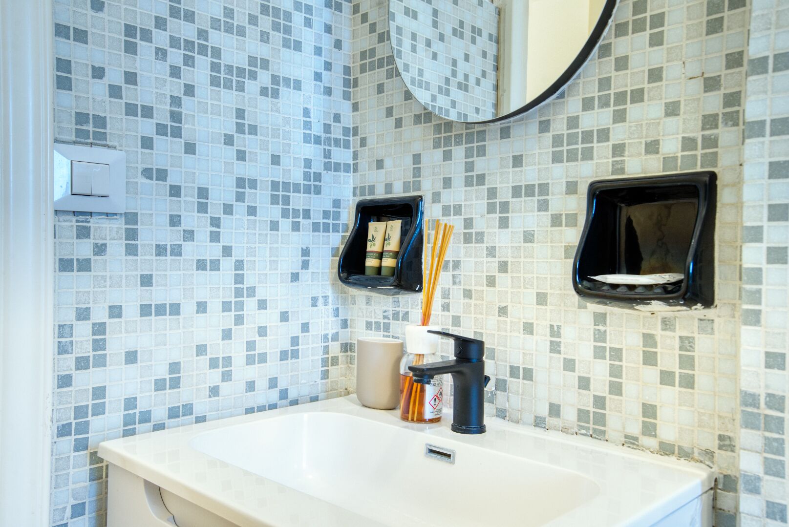A bathroom with a white sink, tiled walls, and two black soap dispensers mounted on the wall.