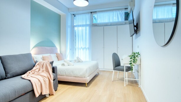A modern bedroom with a grey sofa, a bed with white bedding, a small table with a plant, and a TV mounted on the wall. - Italianflat - Elegant Suites (Milan)
