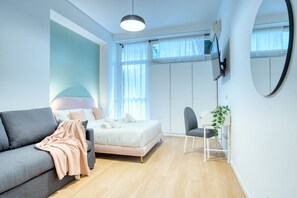 A modern bedroom with a grey sofa, a bed with white bedding, a small table with a plant, and a TV mounted on the wall. - Italianflat - Elegant Suites  (Milan)