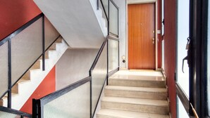 A staircase with a wooden door at the top, a glass railing on one side, and a red wall on the other. - Italianflat - Elegant Suites (Milan)