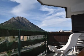 Uma varanda com cadeira branca, vista de montanha e cerca de rede verde.