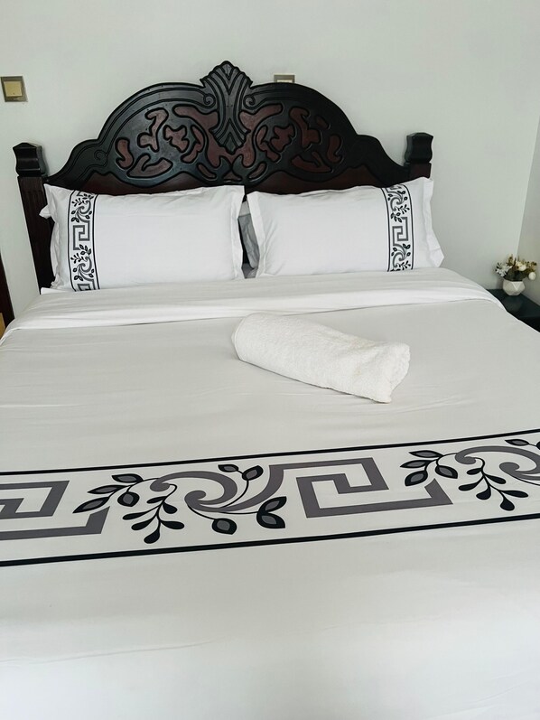 A neatly made bed with a decorative headboard, white bedding, and a patterned bedspread.