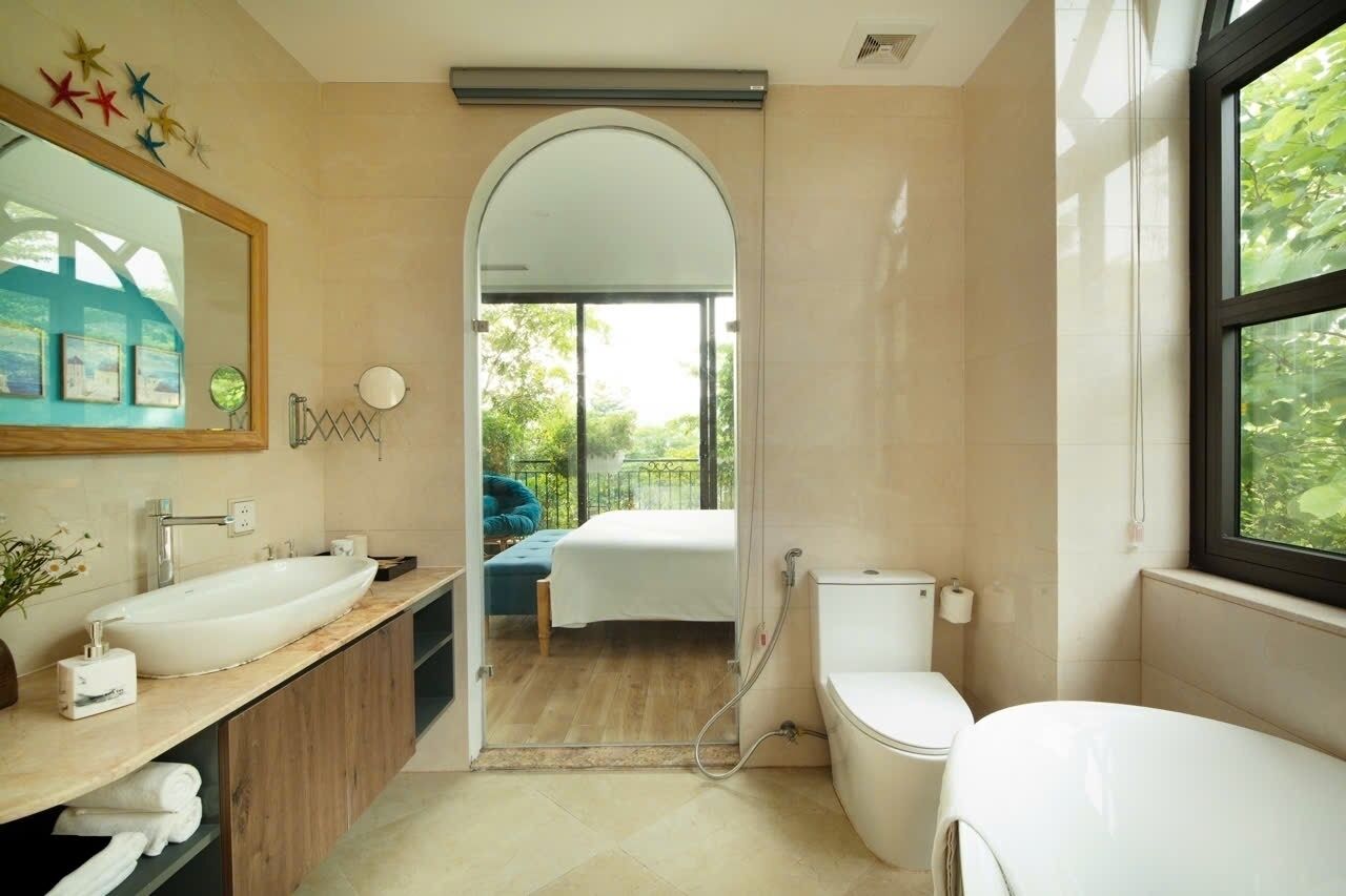 Et moderne badeværelse med stor vask, toilet og brusebad. Et spejl er placeret over vasken, og der er et vindue på højre side.