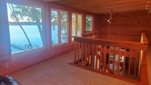 Amplia habitación con ventanas grandes, techo de madera y vista a un cuerpo de agua.