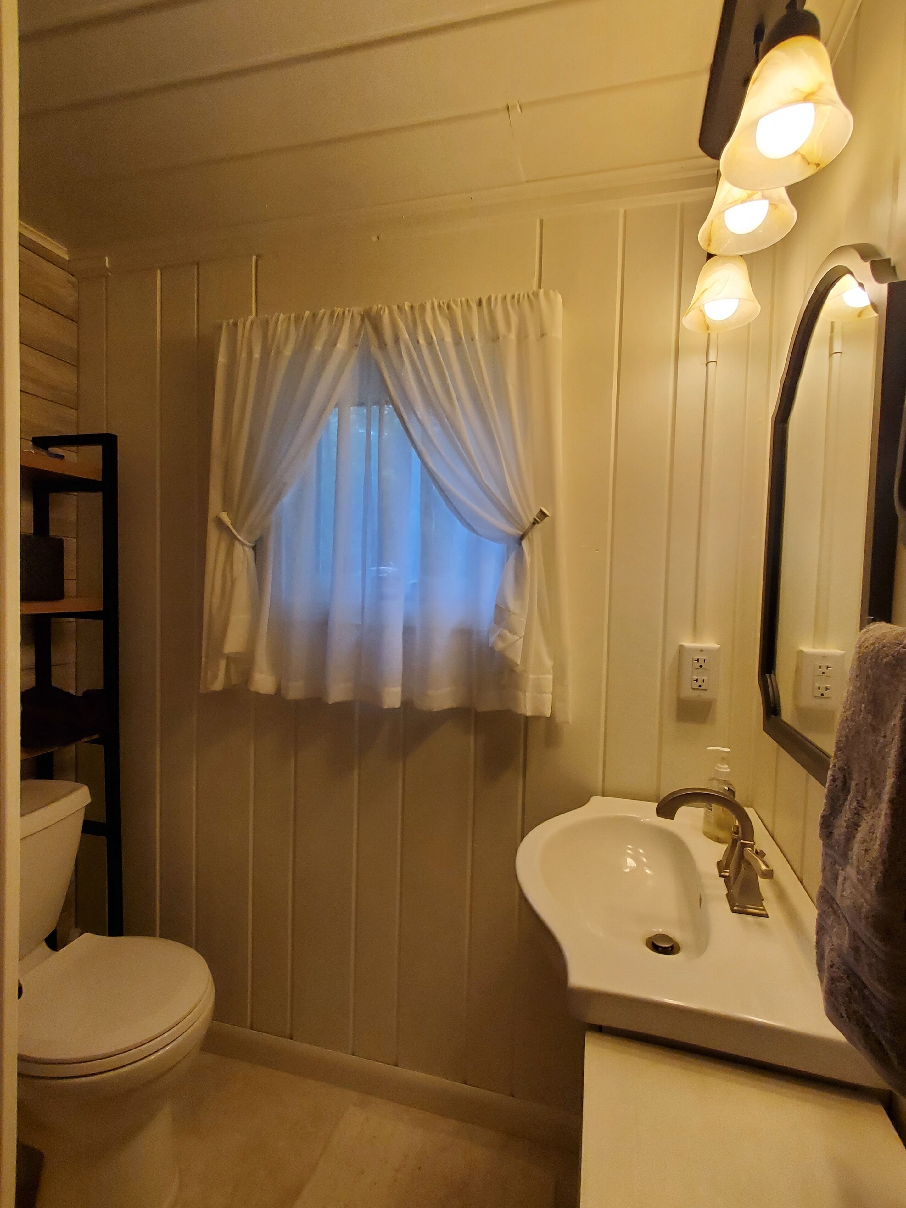 Un baño con inodoro, lavamanos y ventana con cortinas.