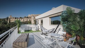 A rooftop terrace with a view of ancient ruins, white furniture, and potted plants. - Acropolis Gate (Athina)