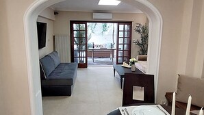 A living room with a sofa, a dining table set for two, and a view through an open doorway to an outdoor patio area. - Acropolis Gate (Athina)