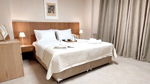 A hotel room with a large bed, wooden headboard, two bedside tables with lamps, a framed picture on the wall, and a window with curtains. - Acropolis Gate (Athina)