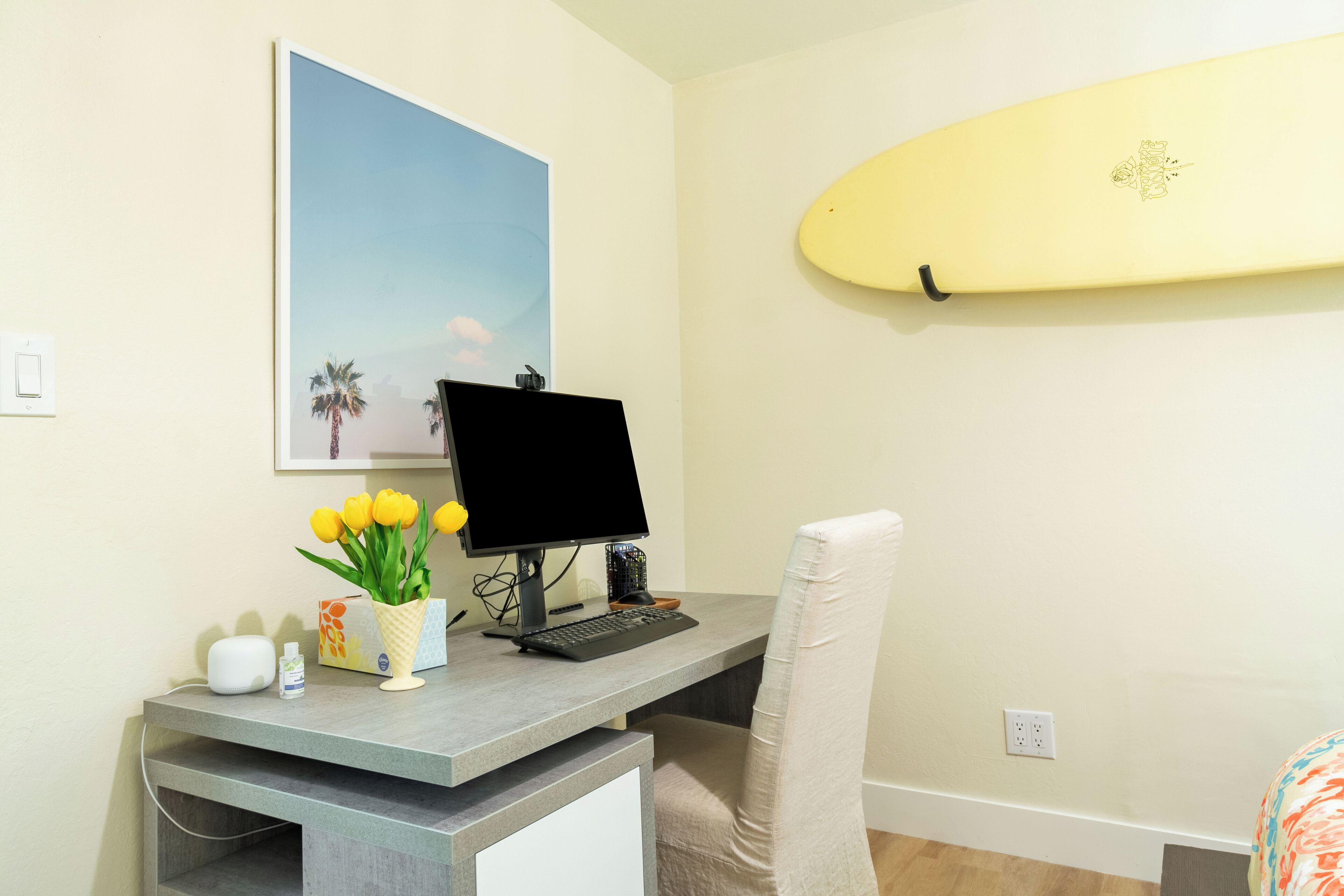 A home office with a desk, computer, and a surfboard on the wall.