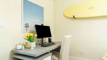 A home office with a desk, computer, and a surfboard on the wall.