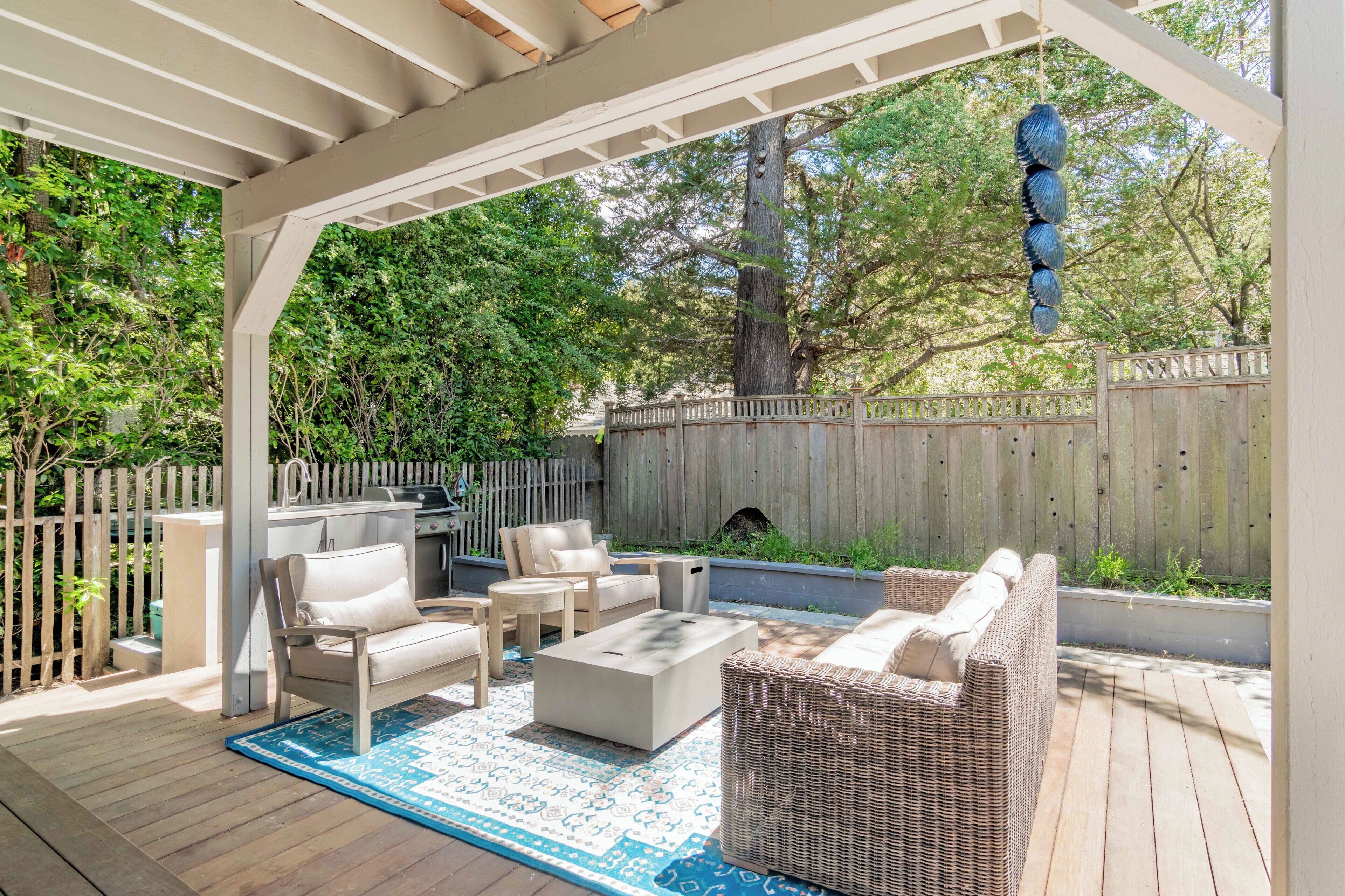 A covered patio area with outdoor furniture, a grill, and a wooden fence.