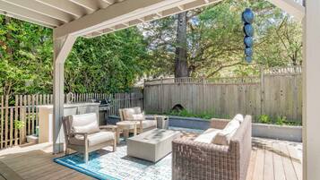 A covered patio area with outdoor furniture, a grill, and a wooden fence.