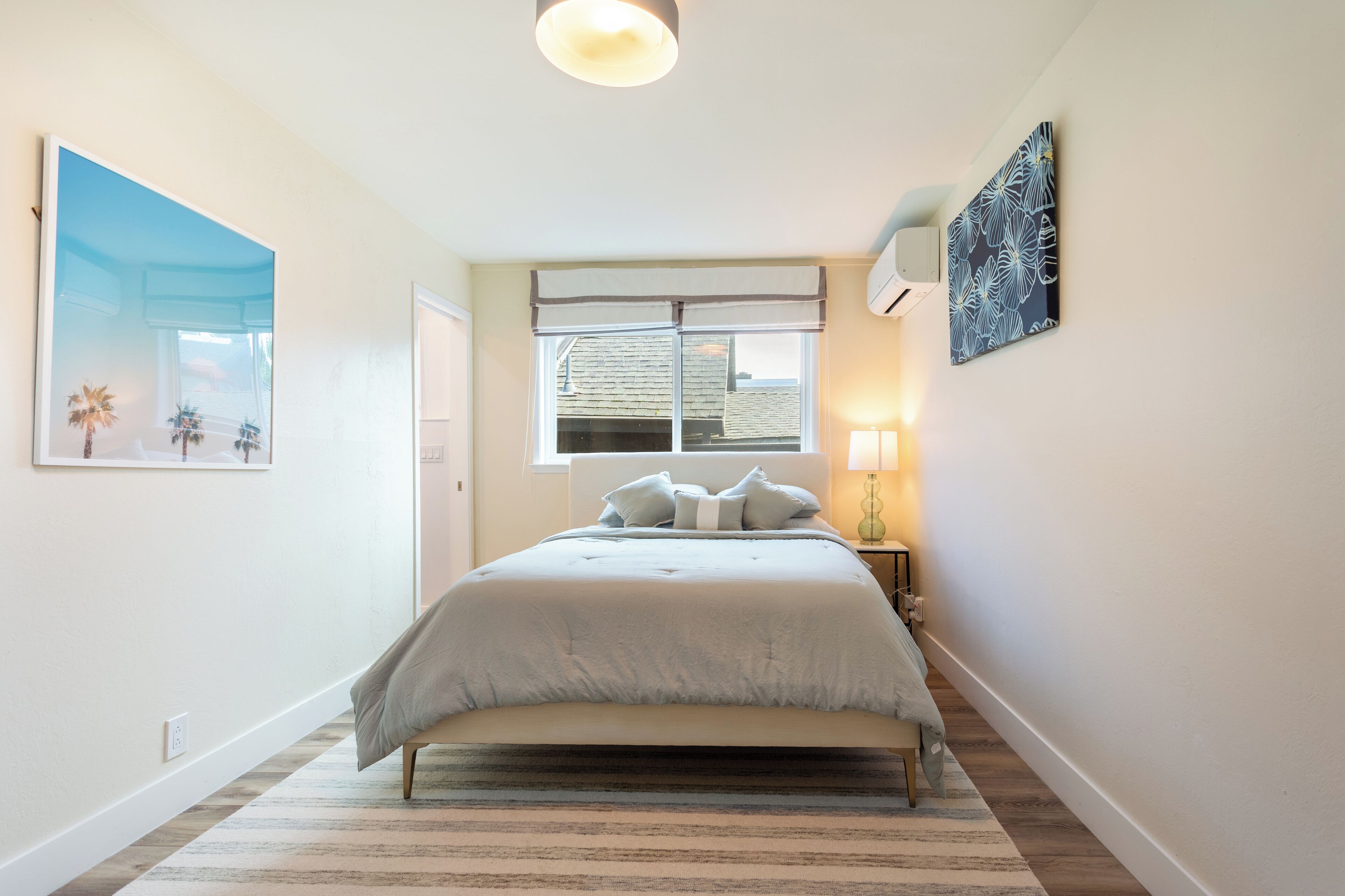 Un dormitorio con cama, ventana, lámpara y aire acondicionado de pared.