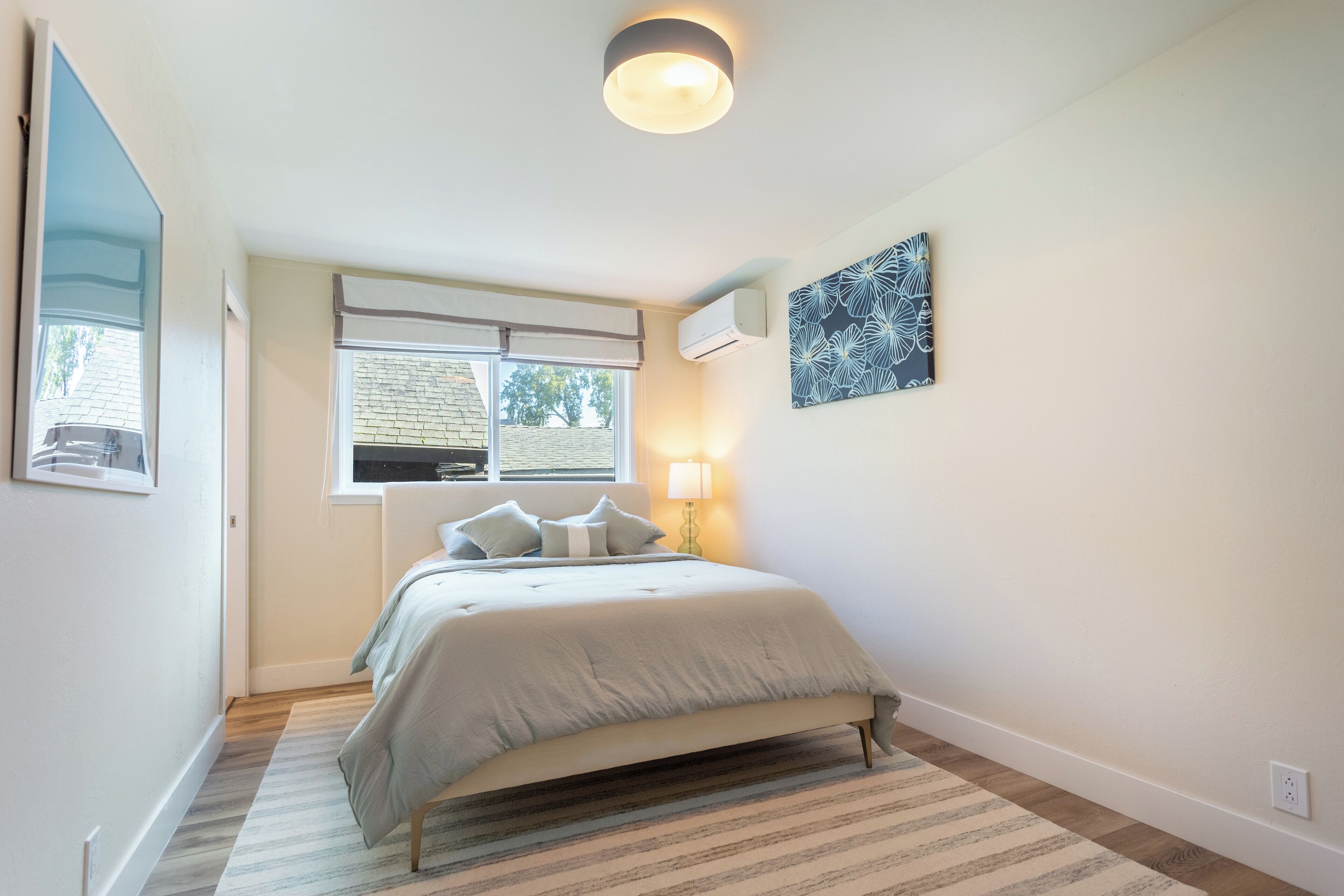 Une chambre à coucher avec un lit, une fenêtre, un climatiseur fixé au mur et une lampe.