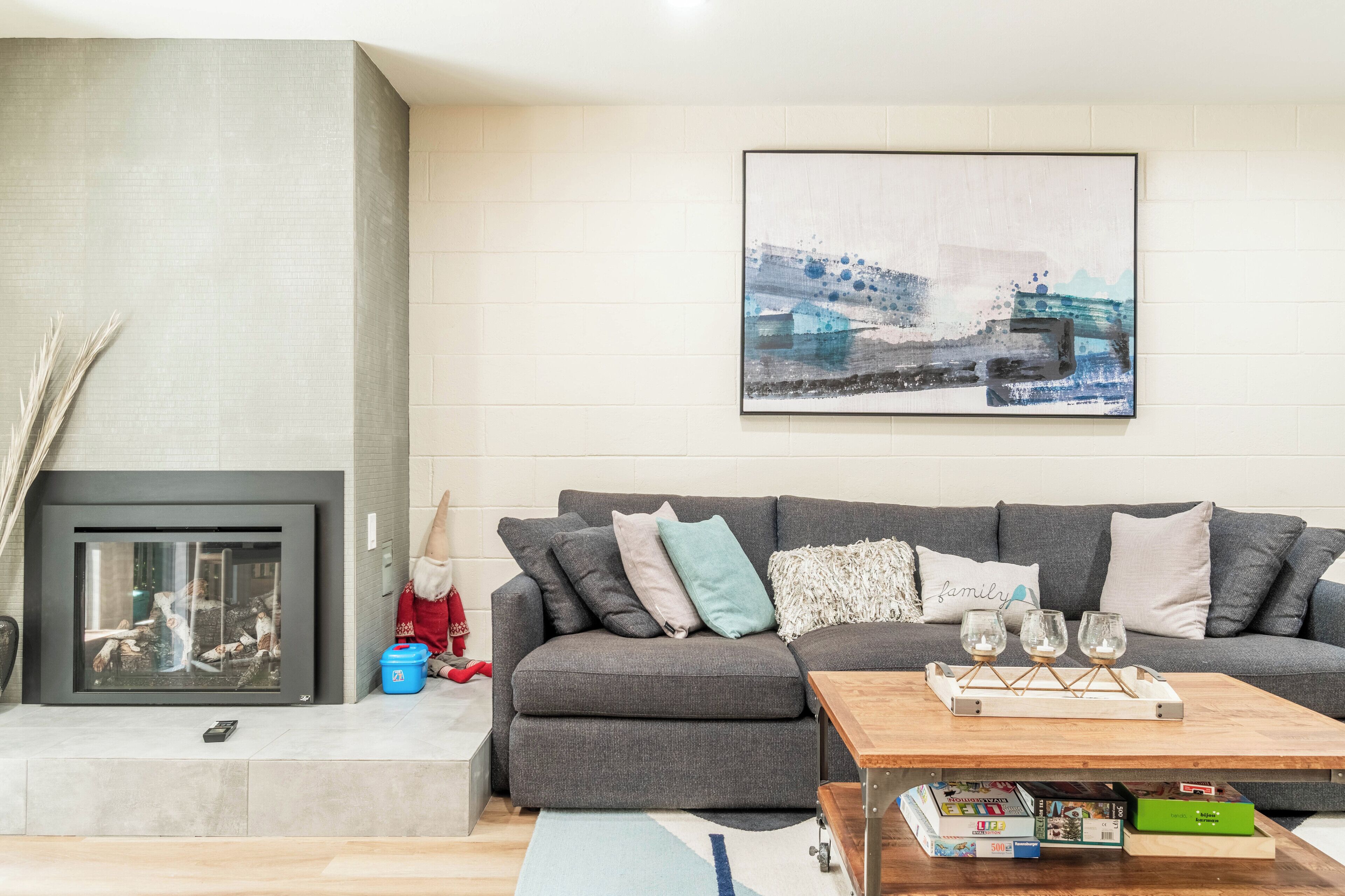 A modern living room with a grey sofa, a fireplace, and a cityscape painting.